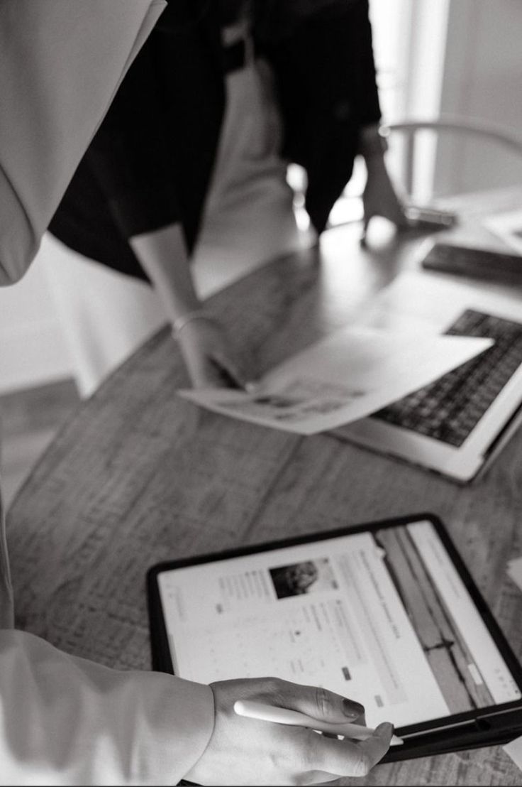 Reviewing printed pages and a tablet together at a meeting table, black and white